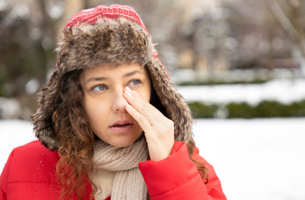 A young woman in a winter coat rubbing her left eye with her left hand.