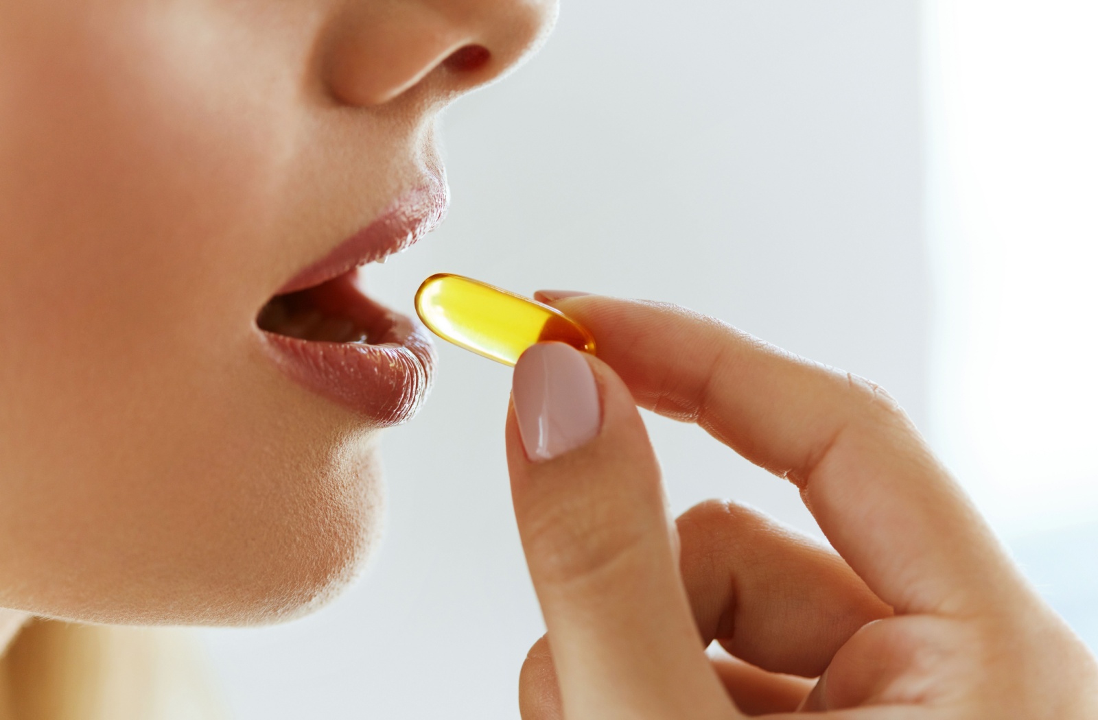 A close-up of a woman taking a vitamin A supplement.
