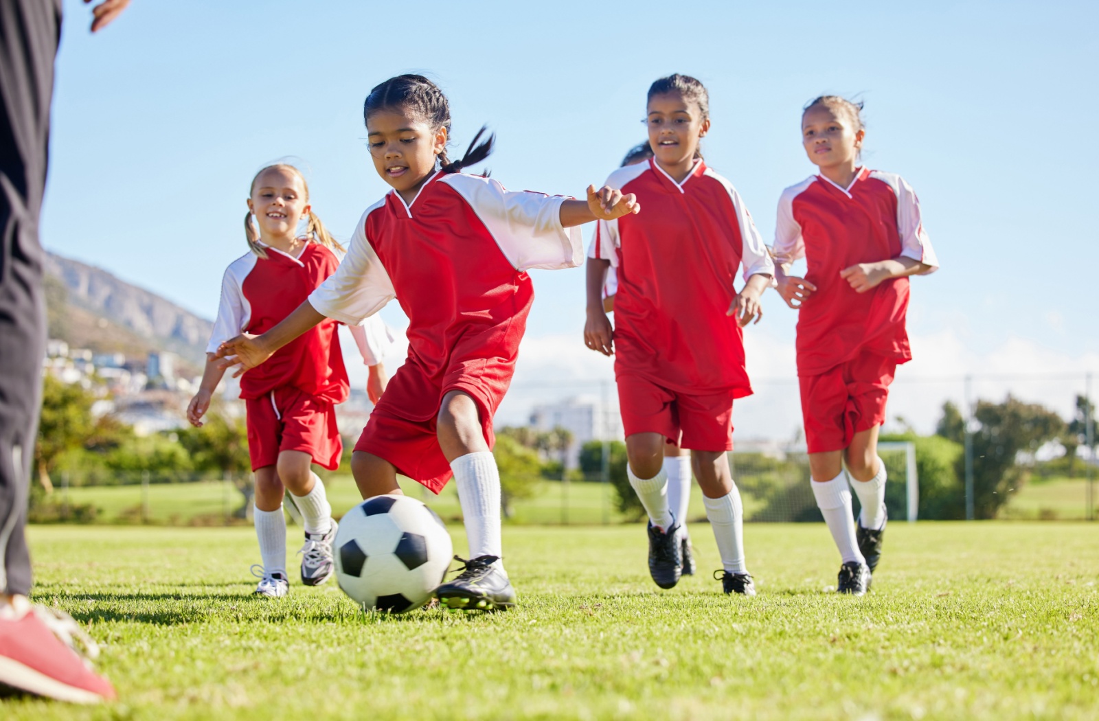 Four members of a young girl’s soccer team chase after a soccer ball on a field during practice.