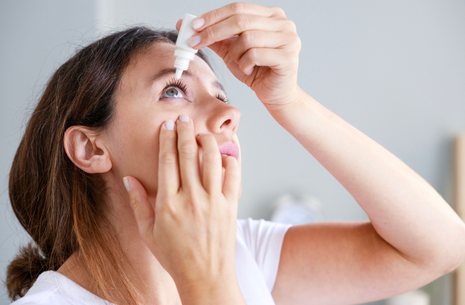 A woman using eye drops for her dry eyes as part of a treatment plan that includes wearing eye masks.