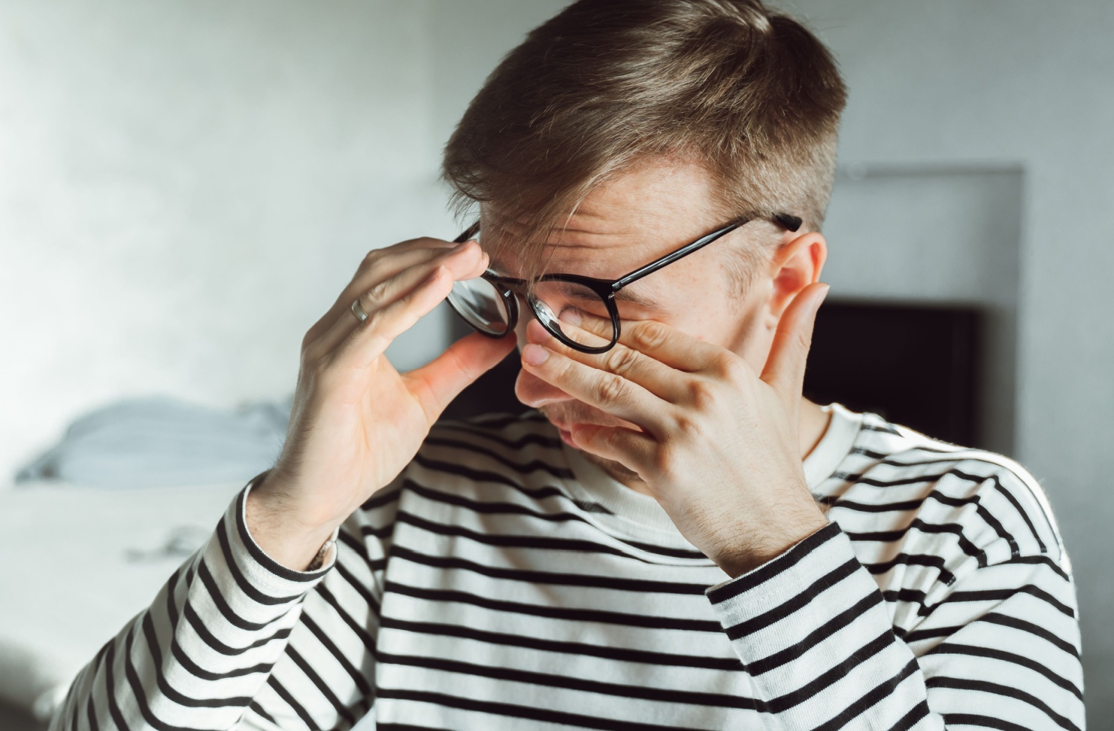 An adult lifts their glasses to furiously rub their itchy eyes.