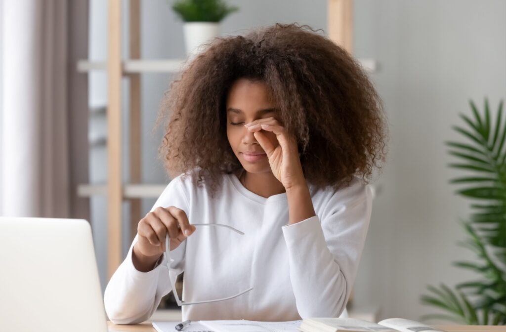 An adult takes a break from working on their computer to rub their tired eyes.