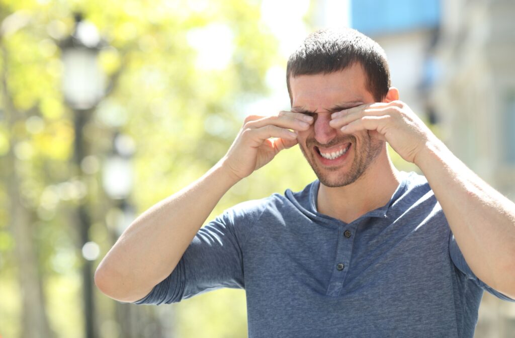 An adult rubs their eyes while outside, grimacing at the pain their dry eye symptoms are causing