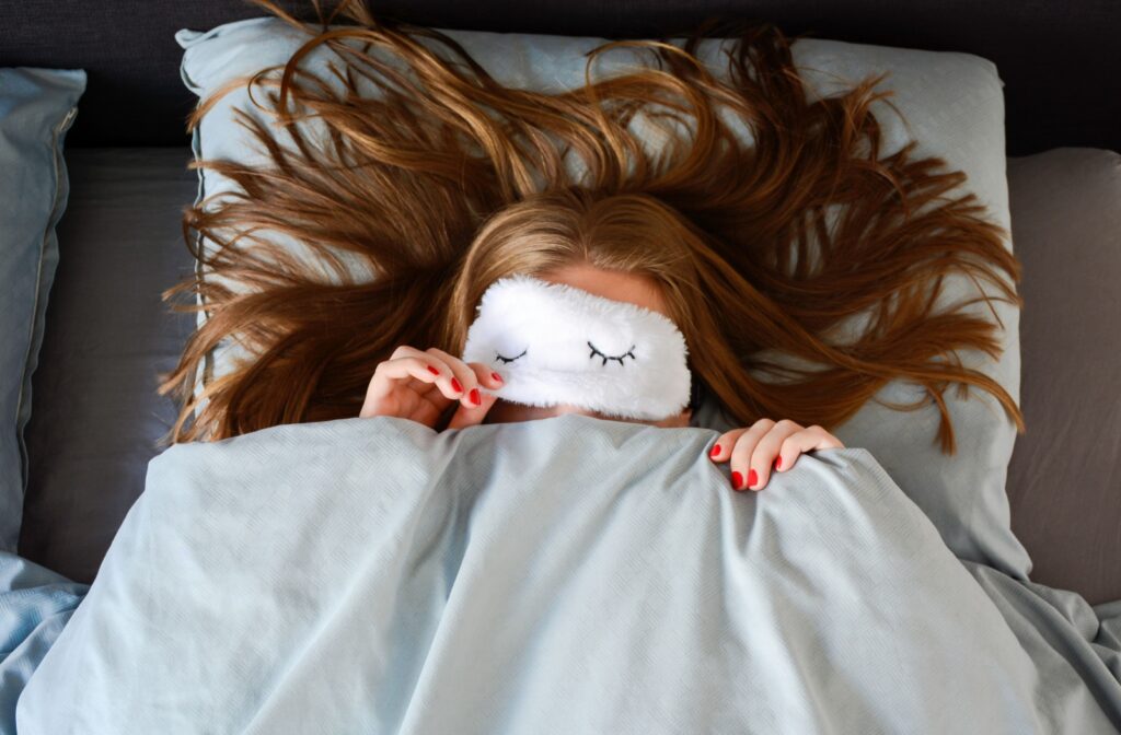 An adult with red nails poised to remove a sleeping mask upon waking up in the morning